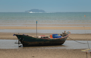 fisherman's fishing boat on sand at a fishing village beach There is an island and sea background with the daytime sky. stranded fishing boat After the sea has receded