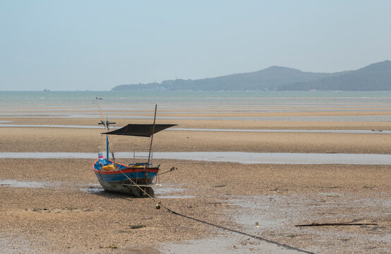 fisherman's fishing boat on sand at a fishing village beach There is an island and sea background with the daytime sky. stranded fishing boat After the sea has receded