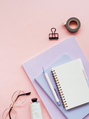 Colorful home office desk workspace with various notebooks and stationery on pink background.