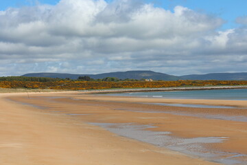 Fototapeta na wymiar A beautiful view of the sandy coastline along the scottish coastline of Dornoch, in the highlands of Scotland. It is a sunny day with blue sky.