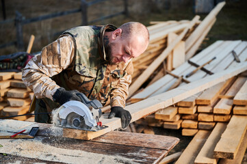 Carpenter using circular saw for cutting wood beam. Man worker building wooden frame house. Carpentry concept.