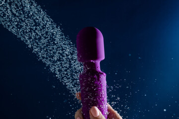 A woman washes a purple vibrator under the shower. Waterproof sex toy on a blue background.