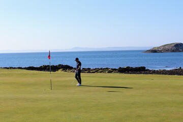 A man putting on a golf green on a links golf course with the ocean in the background on a...
