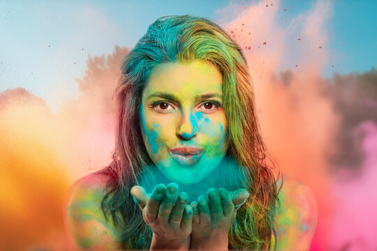Young woman blowing holi powder from hands to camera. Happy woman covered in rainbow colored powder celebrating the festival of colors