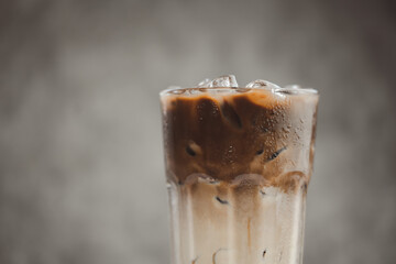 Ice coffee in a tall glass with cream poured over against gray background with copy spec