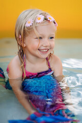 Happy Adorable Little blonde toddler girl with mermaid bathing suit in splashing water while swimming in a inflatable pool on back yard. vertical photo