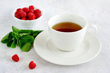 cup of tea with mint leaves and bowl of raspberries, close up  