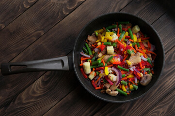 a lot of frozen vegetables in a frying pan on the table. variety of sliced ​​ingredients on a wooden background. juicy fresh vegetables. cooking concept