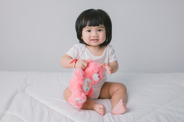 Happy Little Baby Girl Sitting On Bed with pink bear In Bedroom At Home.