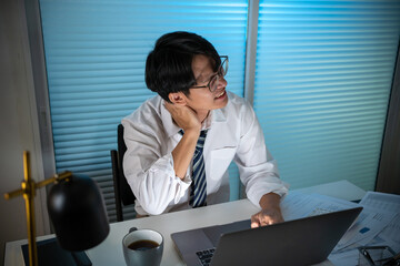 Tired Asian business man falling asleep at table Alone Working Late at Night.on laptop computer at night in dark office. works in the later time