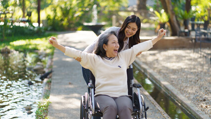 Obraz premium Asian senior woman in wheelchair with happy daughter. Family relationship retired woman sitting on wheelchair in the park age care at retirement home.