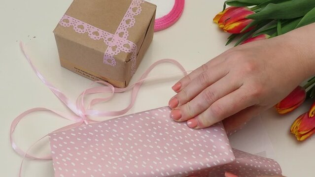 Mother's Day concept. Top view photo of stylish pink giftbox with ribbon bow and bouquet of tulips on isolated pastel pink background. girl wrapping a gift