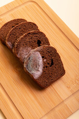 Spoiled rotten moldy rye brown bread on wooden desk from above on light beige background.