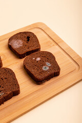 Spoiled rotten moldy rye brown bread on wooden desk from above on light beige background.