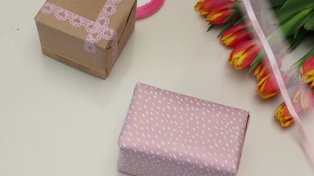 Mother's Day concept. Top view photo of stylish pink giftbox with ribbon bow and bouquet of tulips on isolated pastel pink background. girl wrapping a gift