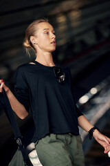 Pretty young fitness girl getting ready for a workout at the stadium. Attractive slim blonde in a black T-shirt and green cargo pants with a sports bag goes to the locker room. Active lifestyle.