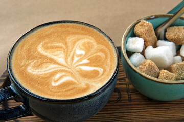 Blue Ceramic Cup of Hot Cappuccino with Flower Shaped Foam on Wooden Cafe Table. Beautiful Latte Art Froth. Trendy Authentic Modern Porcelain Set. Pottery Handmade Coffee Mug Served with a Sugar Bowl