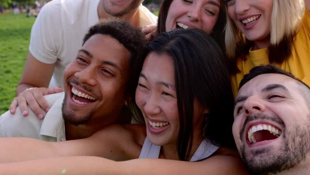 Group of multiracial friends having fun taking selfie with mobile phone while enjoying day off and free time together at city park. Multiethnic people laughing outside. Youth community concept.