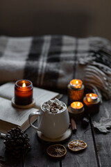 Aromatherapy on a grey fall morning, atmosphere of cosiness and relax. Autumn cozy home composition with hot chocolate with marshmallow and candles. Wooden background, books, close up.