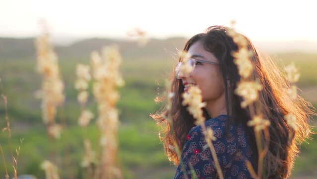 Rear view shot of a beautiful Indian girl sitting on a field and enjoying the nature. Girl in the outdoor during sunset. Travel lifestyle.