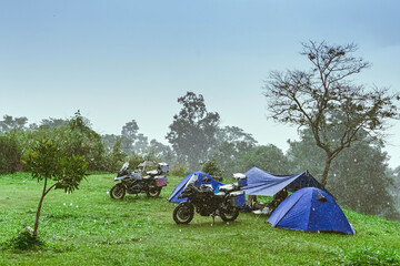 Motorcycle with rain. Camping activity in rain-filled holiday. Tent on campsite by the hill in rainy day. Mountain camp in forest in the rain. Motorcycle tourism in rainy season. Vacation destination.