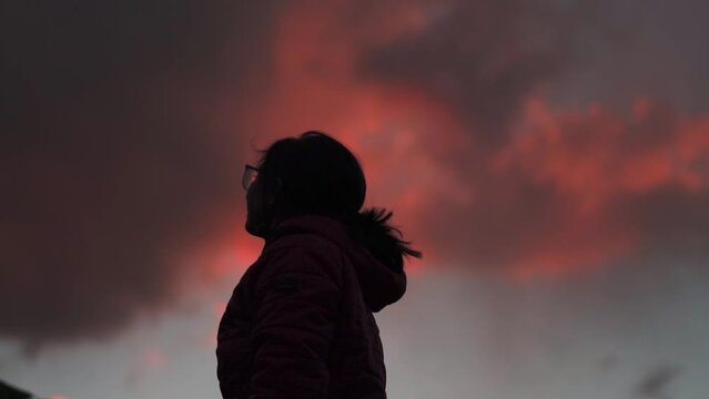 Silhouette of Indian teenager girl looking at orange sky during sunset at Manali, Himachal Pradesh, India. Hopeful girl stares at the sky. Female lost in deep thoughts after looking at the sunset.