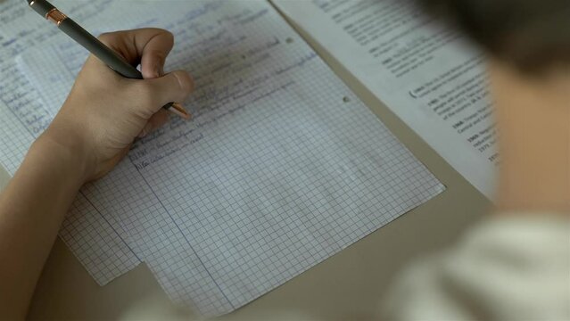 College student making notes, writing on paper on desk at home with laptop and studying