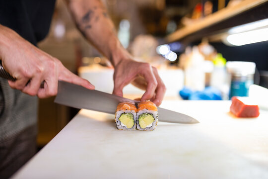 Unrecognizable man cutting fresh sushi with knife