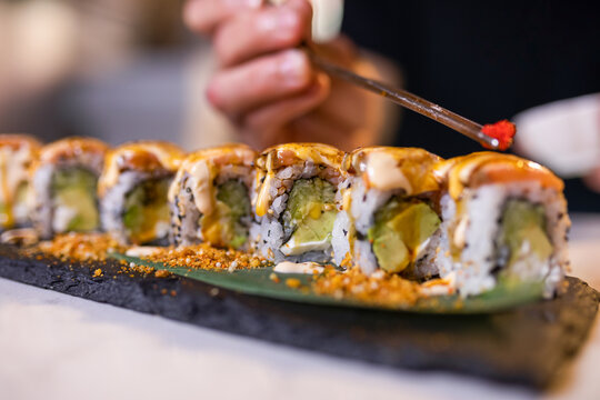 Unrecognizable person serving tobiko on uramaki sushi rolls with chopsticks