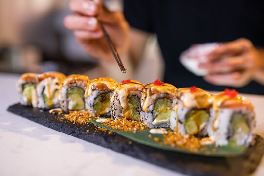 Unrecognizable person serving tobiko on uramaki sushi rolls with chopsticks