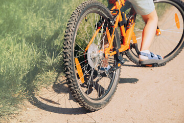 photo of a boy riding an orange bicycle in the park. A warm summer day. Bottom and back view. focus on wheels