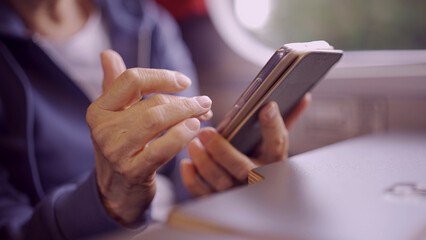 Obraz premium Close-up of the hands of a elderly lady sitting in a train carriageriage and using a smartphone