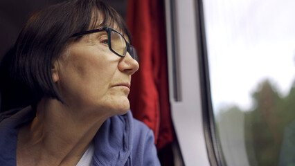 Fototapeta na wymiar Elderly lady in glasses travels in train and looking out the window