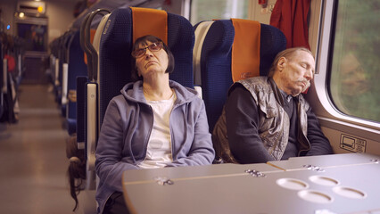 An elderly couple ride the train early in the morning and sleep