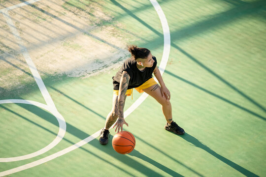 Brutal woman dribbling basketball ball on court