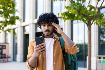 Upset student with backpack reads bad news on phone, man with phone browses internet page on...