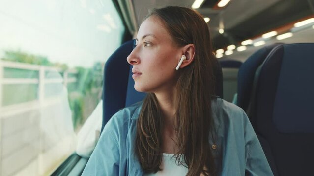 Cute girl with long brown hair, wearing blue shirt, wearing wireless earphone into ear traveling by suburban train