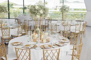 Served wedding tables with golden plates, decorative fresh  white roses and gypsophila flowers and...