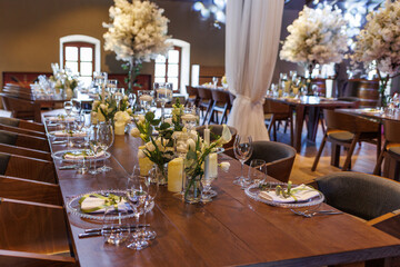 A general plan of a festive tables decorated with a white trees, chairs, plates, compositions of white flowers and candles. Wedding decoration and decor