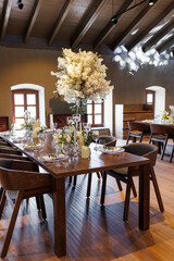 A general plan of a festive tables decorated with a white trees, chairs, plates, compositions of white flowers and candles. Wedding decoration and decor