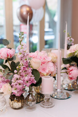 Close up decorative composition of greenery, fresh white and  pink flowers, white candles on a festive table with a white tablecloth. Concept of wedding decorations 
