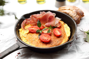 Fresh french omelette with tomato and prosciutto on a cast iron pan, with blurred background.