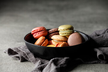 Different macaroons in a black bowl on a towel. Black background, close-up, free space for text	
 - obrazy, fototapety, plakaty