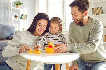 Dad, mom and toddler baby playing toys at home. Cheerful caring parents and kid playing with rubber duck toys together in living room at home. Happy parenthood, childhood concept