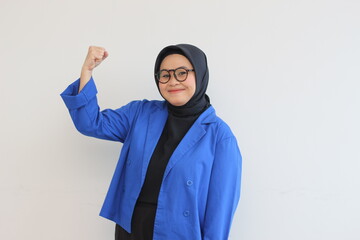 beautiful young Asian Muslim woman, wearing glasses and blue blazer with fists clenched in spirit gesture