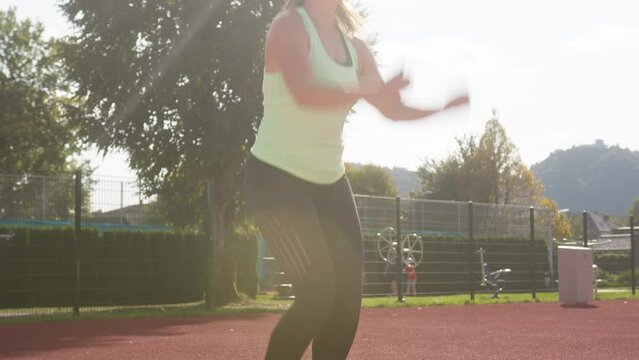 Young female athlete beyond start line, assuming crouching start position and running along a stadium athletic track, handheld shot.