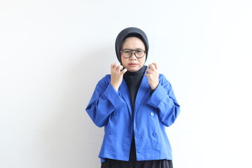 Young beautiful Asian Muslim woman, wearing glasses and blue blazer with angry facial expression