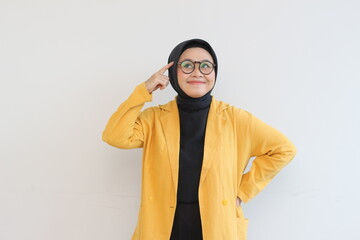 Beautiful young Asian Muslim woman, wearing glasses and yellow blazer is thinking isolated on white background.