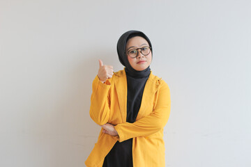 beautiful young Asian Muslim woman, wearing glasses and yellow blazer with hand gesture of approval or OK