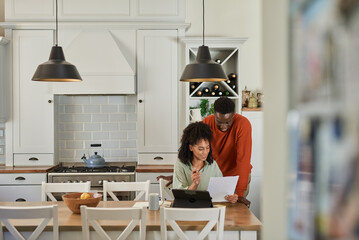 Smiling multiracial couple doing their online banking on a tablet at home